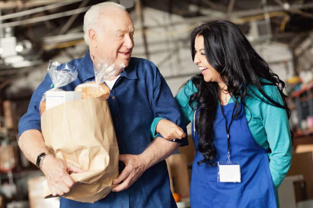 An older gentleman with a grocery bag holding the hand of a woman