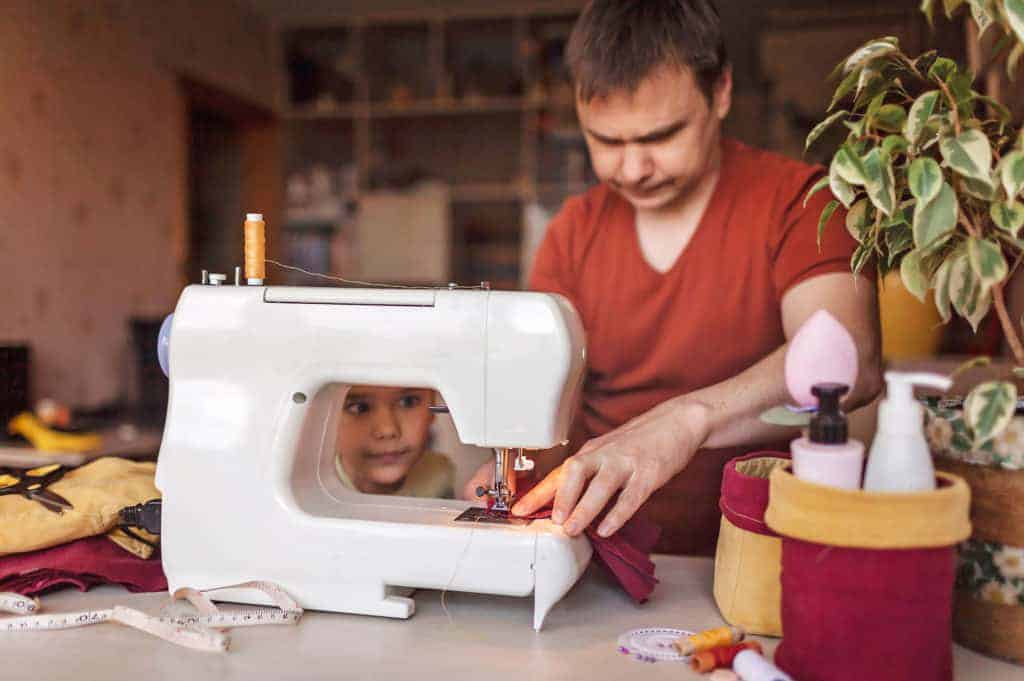 A man using the sewing machine while a child watches